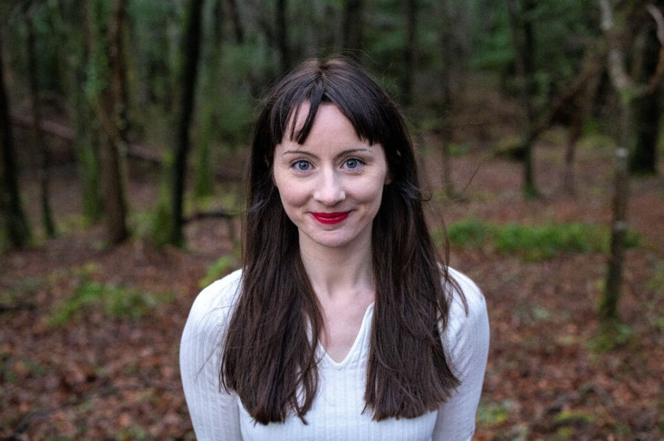 A photograph of a smiling Miriam Needham taken in a forest.