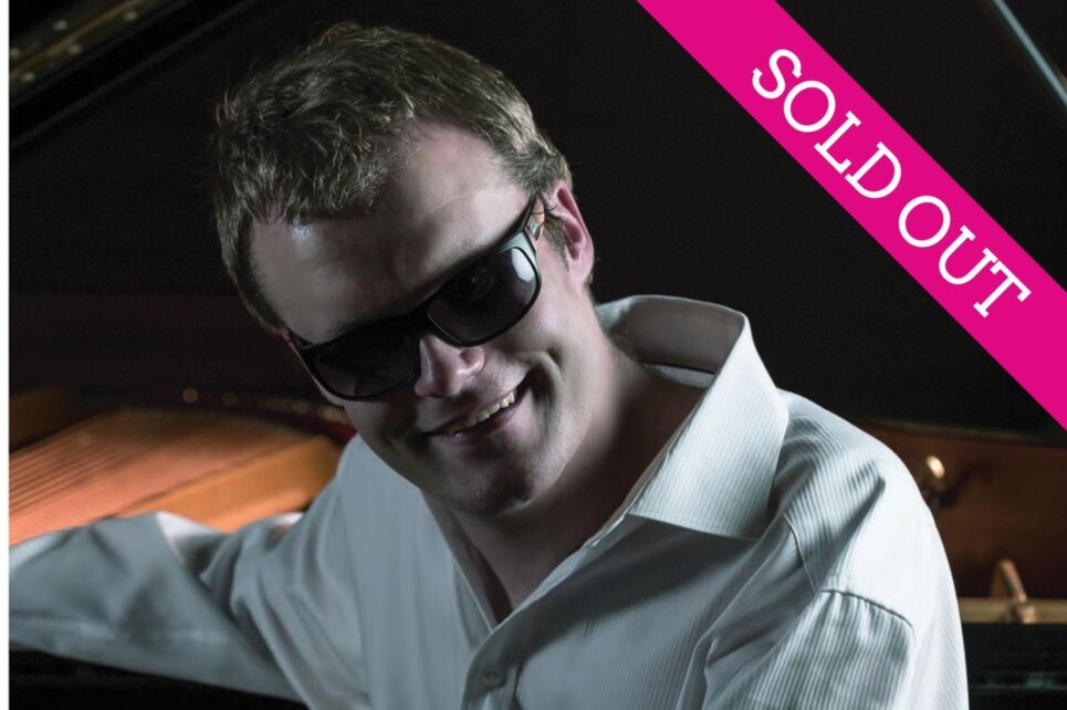 Artist Derek Paravicini sitting at his piano wearing sunglasses