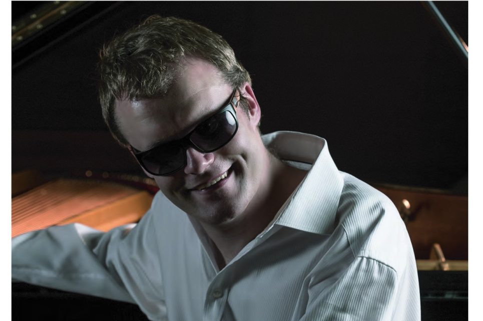 Artist Derek Paravicini sitting at his piano wearing sunglasses 