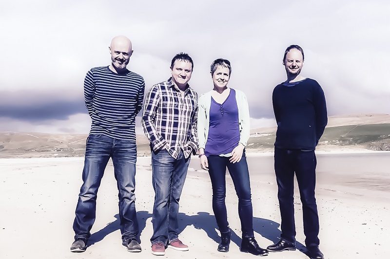 A photograph of the members of Flook against a backdrop of a beach and clouds