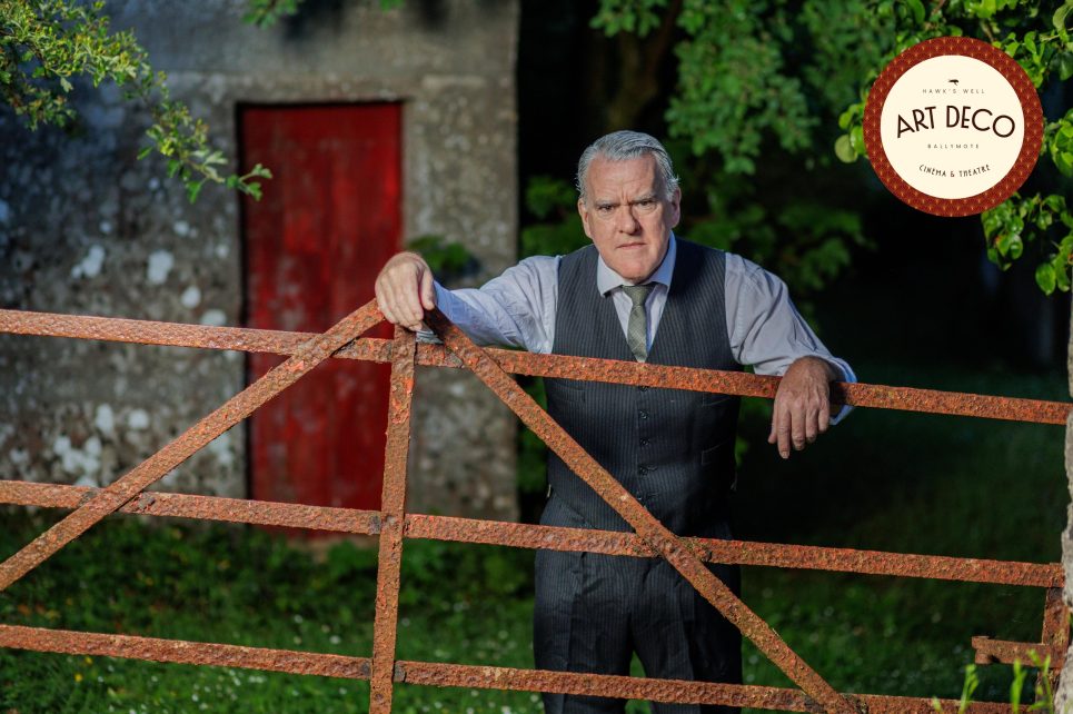Mikel Murfi in a vest and tie stands by a rusty gate outside a stone building with a red door. Mikel Murfi in a vest and tie stands by a rusty gate outside a stone building with a red door.