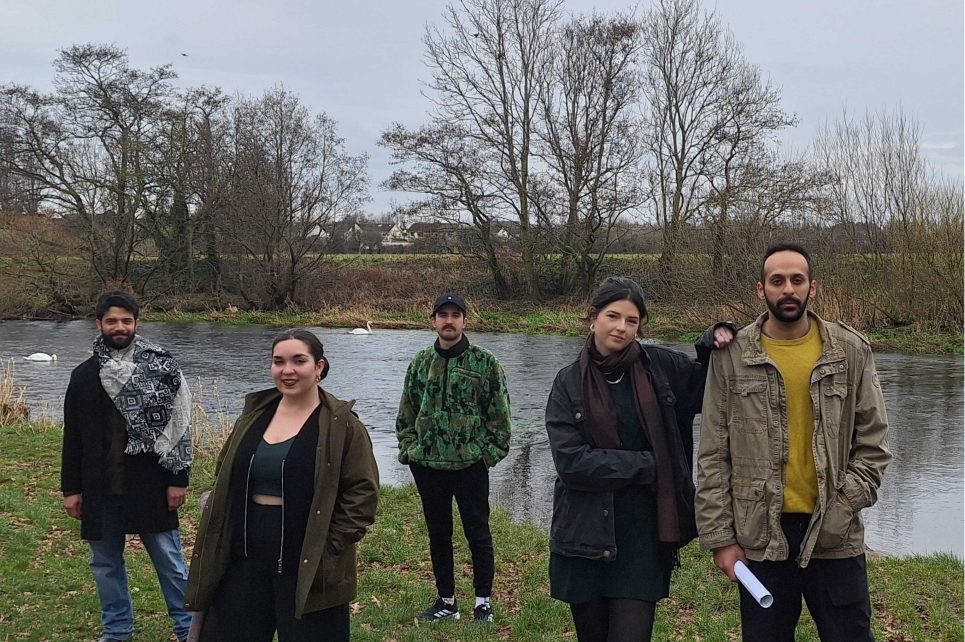 A photograph of the members of Crooked House Theatre Company standing by a small lake.