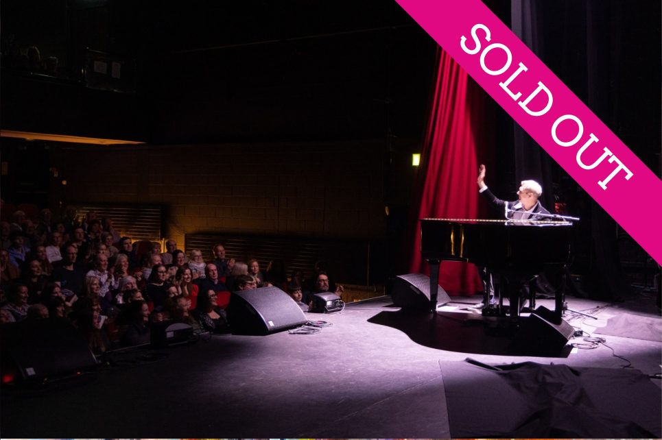 Pianist on stage under spotlight waving at audience