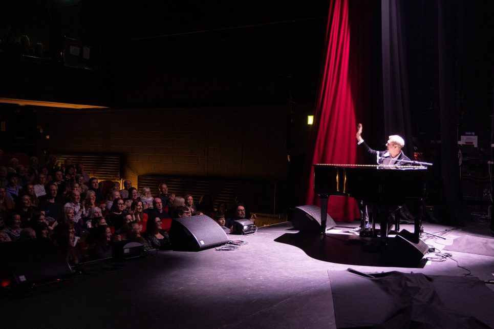 Pianist on stage under spotlight waving at audience