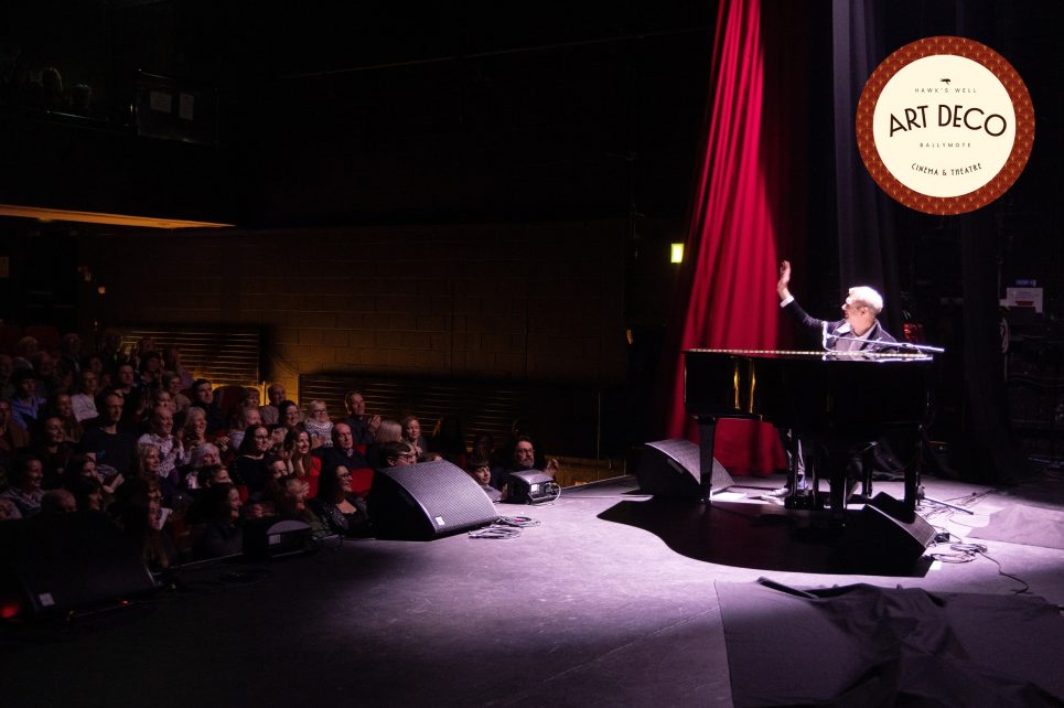 Pianist on stage under spotlight waving at audience