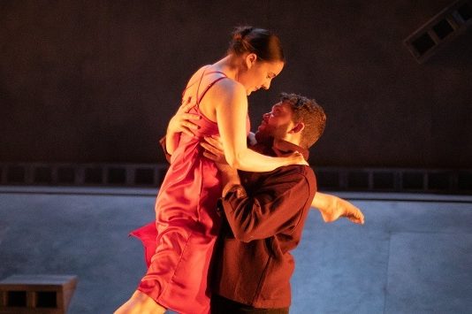 A photograph of a pair of dancers on stage. The man is holding up the woman in a performance pose
