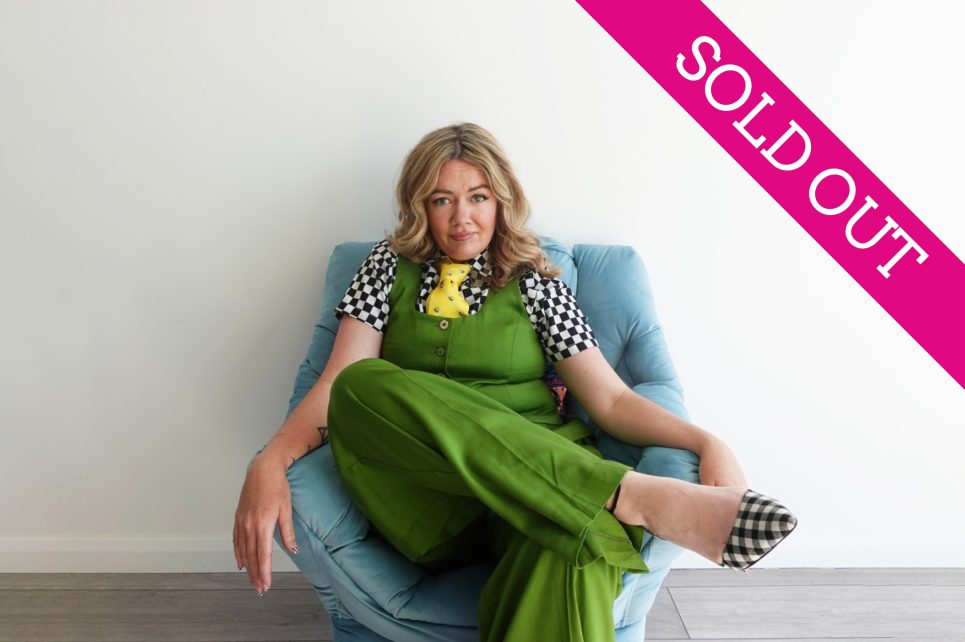 Comedian Serena Terry sitting on a chair wearing green against a white wall