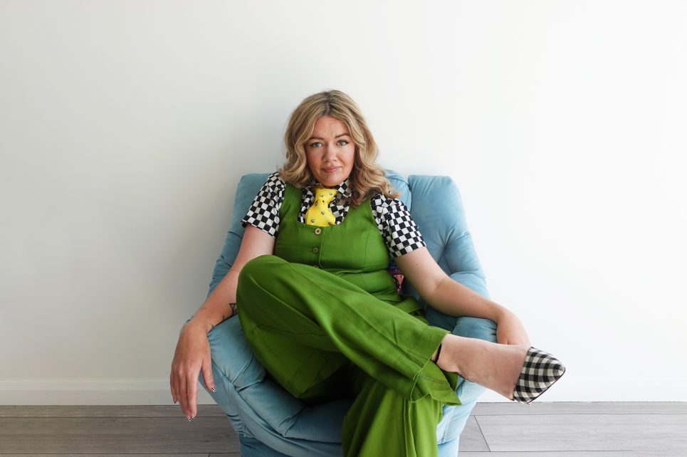 Comedian Serena Terry sitting on a chair wearing green against a white wall  Comedian Serena Terry sitting on a chair wearing green against a white wall