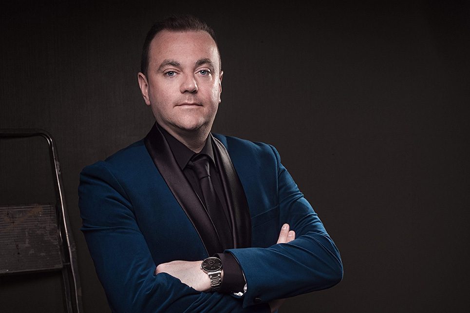 A photograph of Patrick Feeney in a dark blue suit and his arms crossed over his chest.