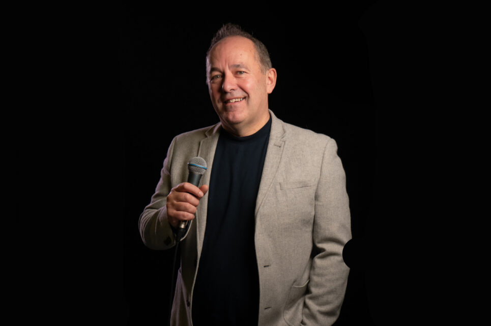 Shane Martin with a microphone on a black background
