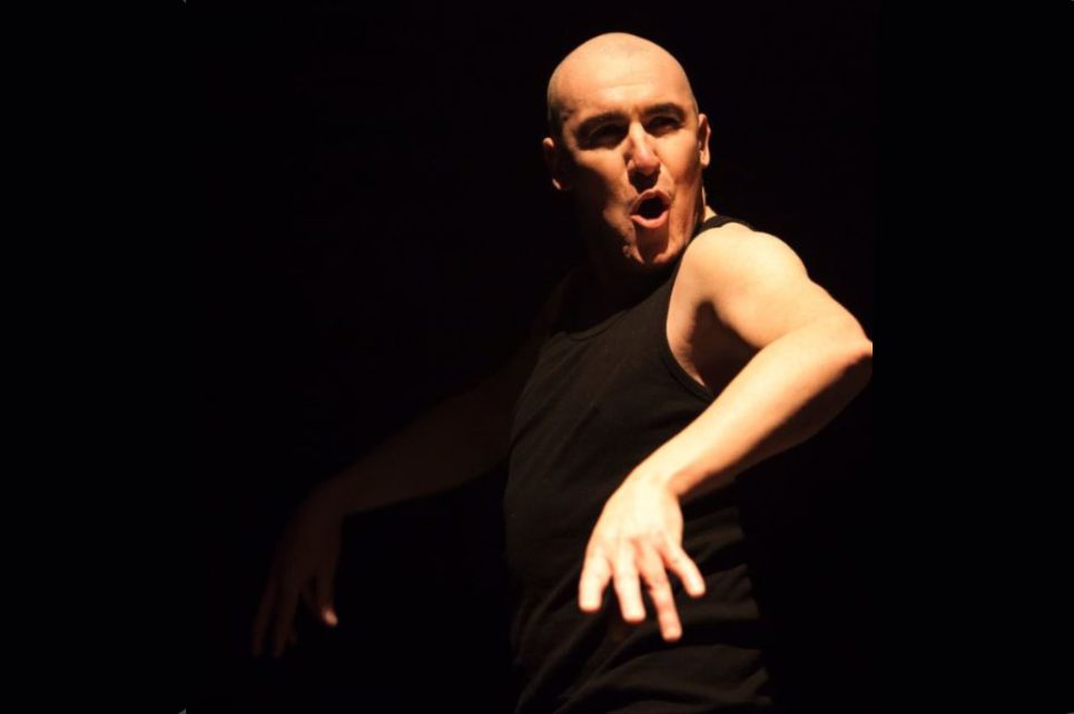 Pat Kinevane on stage, set against a black backdrop