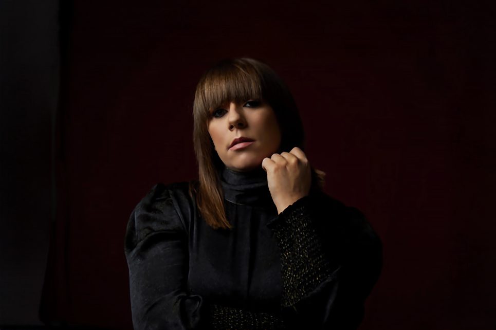 Singer Stephanie Rainey wearing a black outfit against a dark red background  Singer Stephanie Rainey wearing a black outfit against a dark red background