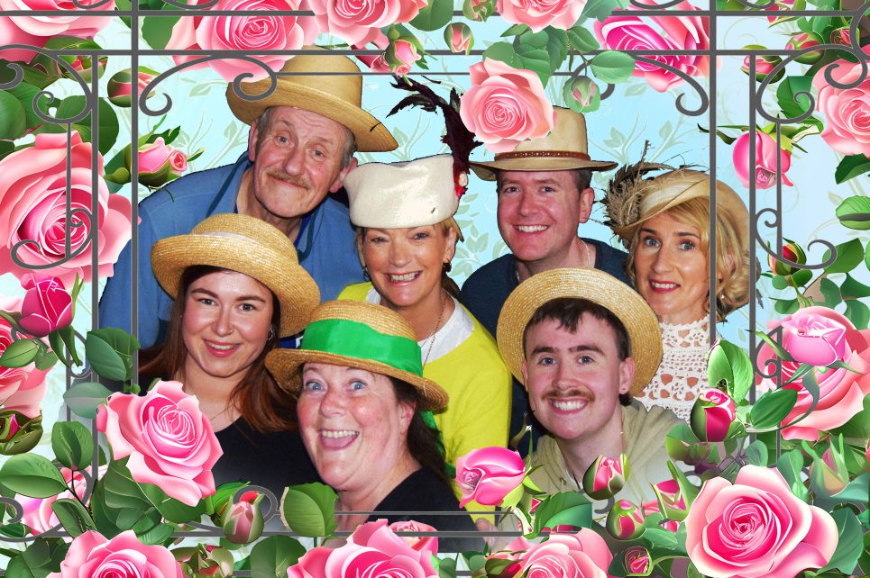 A photograph of members of the Sligo Drama Circle smiling and wearing straw hats. The image is framed by pink roses.  A photograph of members of the Sligo Drama Circle smiling and wearing straw hats. The image is framed by pink roses.