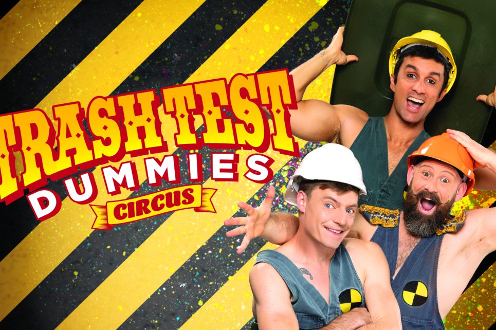 Three performers standing in a wheelie bin wearing hard hats